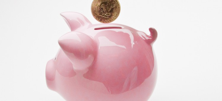 Hand dropping a loonie into a pink piggy-bank
