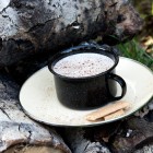 latte in black cup on white saucer on cord of wood