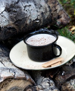 latte in black cup on white saucer on cord of wood