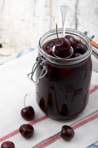 jar of pickles cherries, with cherries loosely layout outside of the jar