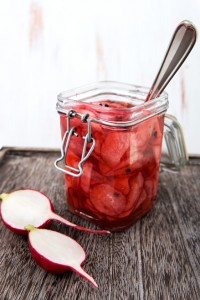 jar of pickled radishes, with spoon in jar and on a serving platter