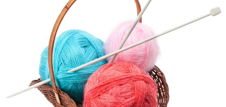 Three balls of wool in basket with knitting needles